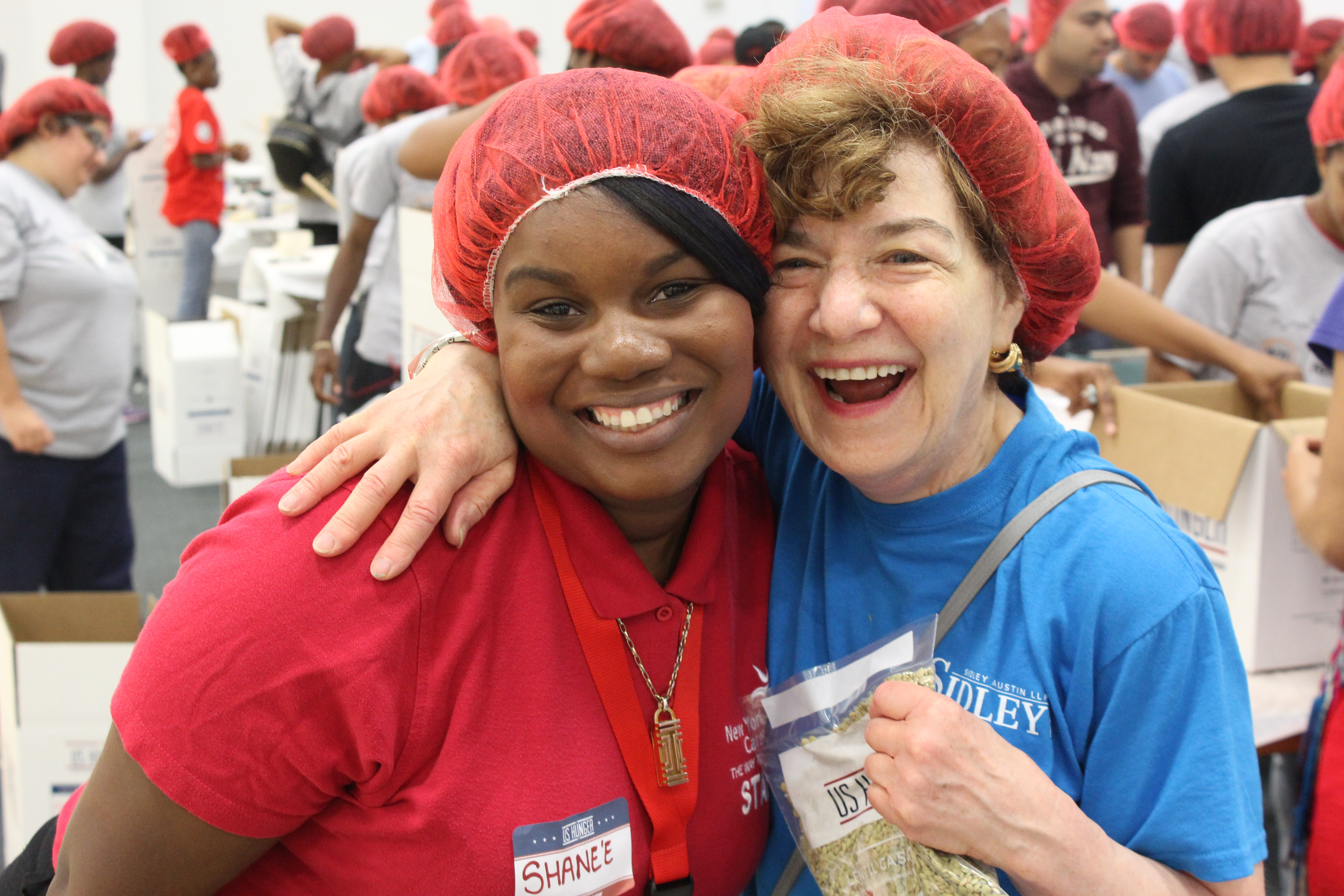 Two women in hairnets hug and smile