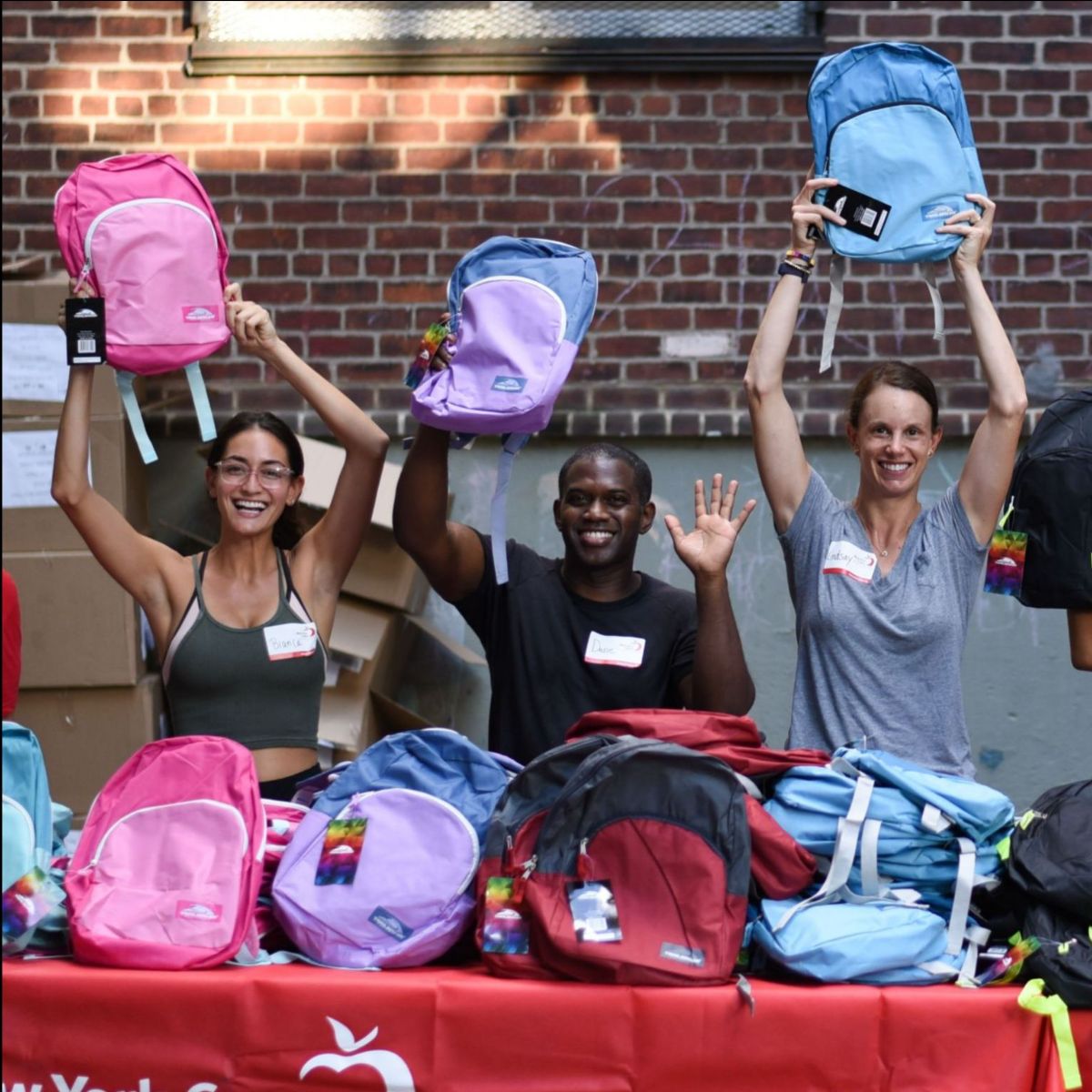 Three individuals hold backpacks above their heads during a volunteer sorting project