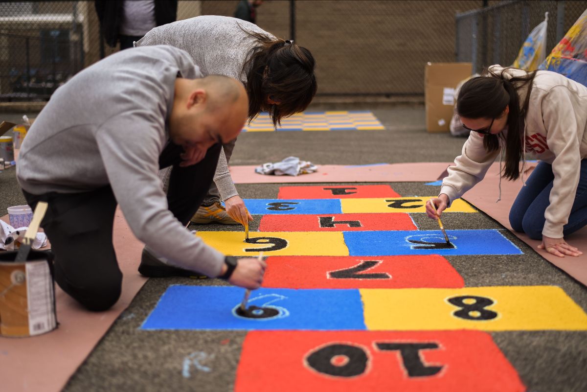 Three individuals paint a hopscotch board on a rug