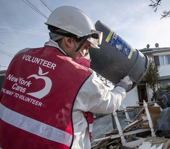 Man wearing hard hat and New York Cares vest emptying garbage