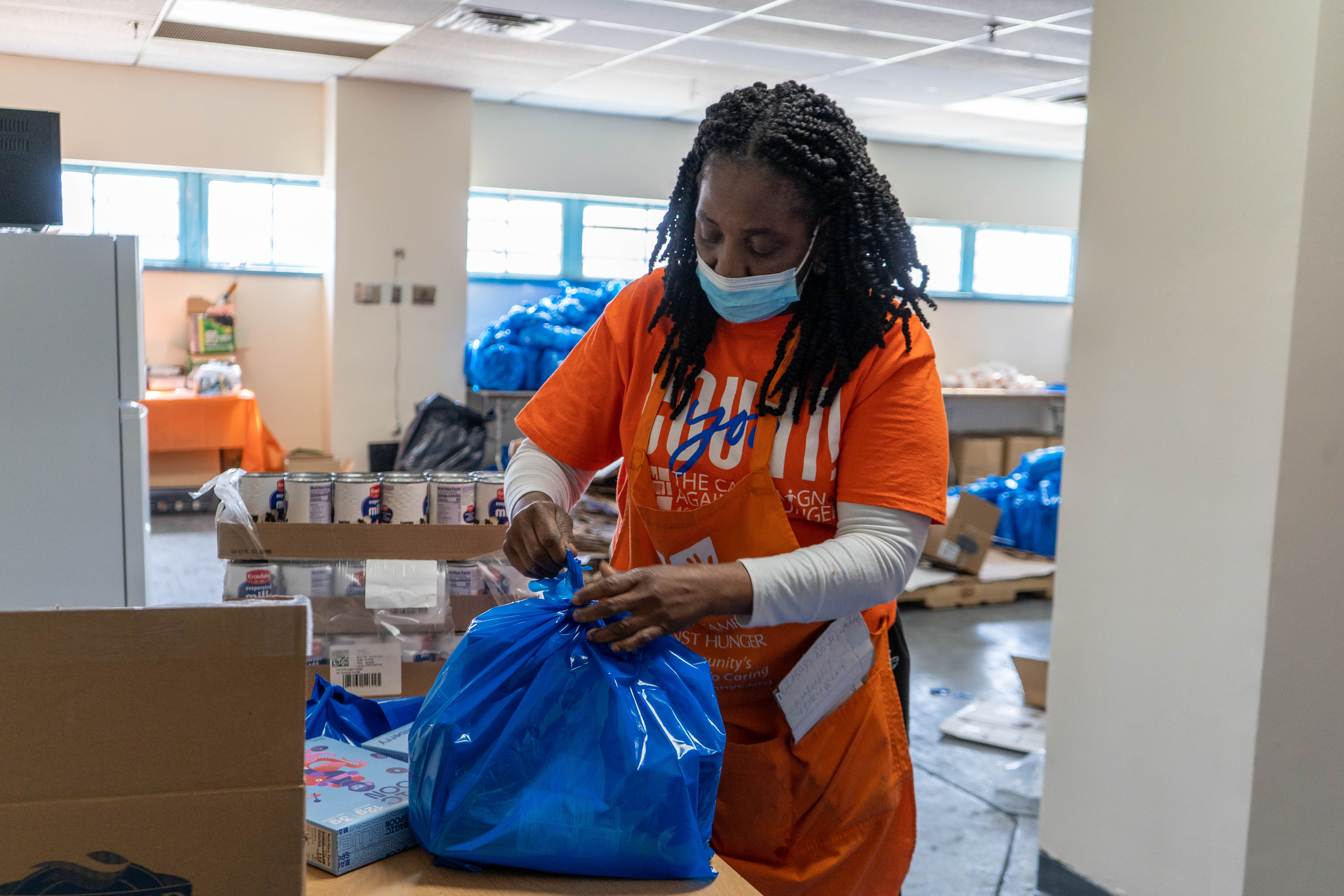 A woman in an orange shirt and a mask ties a blue plastic bag